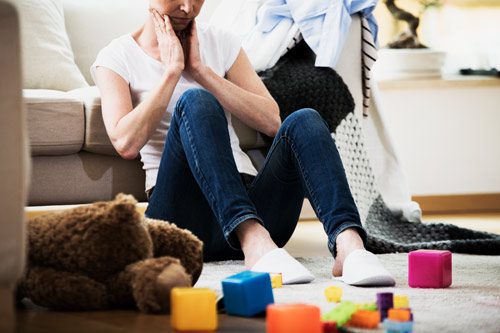 overwhelmed woman sitting on floor in living room with children's toys - functioning alcoholic