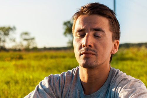 man outside with eyes closed meditating - mindfulness