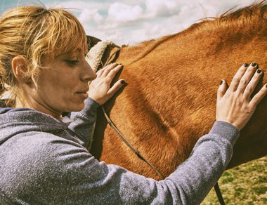 woman petting tan colored horse