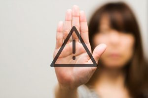 black triangle with exclamation point against woman holding out her hand in stop gesture - relapse warning signs