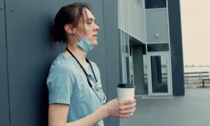 stressed doctor or nurse outside on break drinking coffee - High-Functioning Addiction