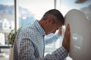 What Is Dry Drunk Syndrome? Signs & Symptom, handsome middle age businessman stressed and leaning his head and hands on a whiteboard at work - dry drunk syndrome
